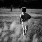 a little boy running through a field of tall grass