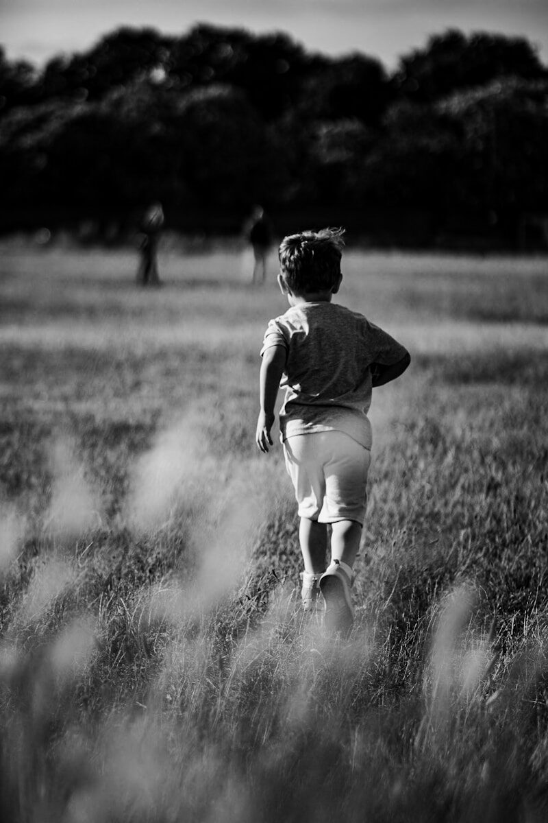 a little boy running through a field of tall grass