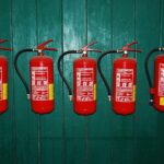 four fire extinguishers lined up against a green wall